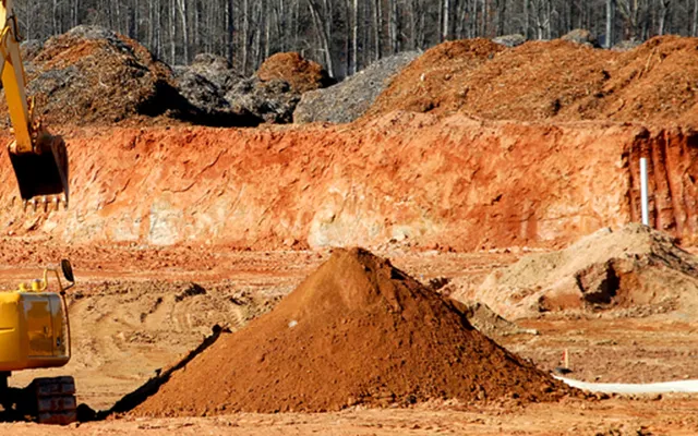Excavator working on a cleared site with banks of red earth