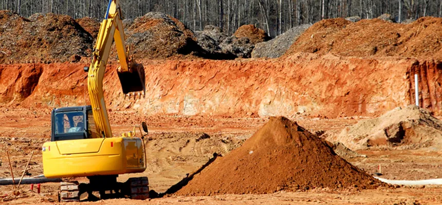 Excavator working on a cleared site with banks of red earth
