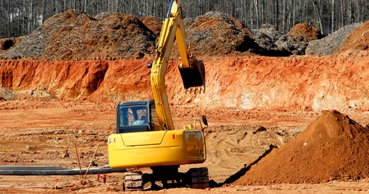 Excavator at work on a cleared site with banks of red earth